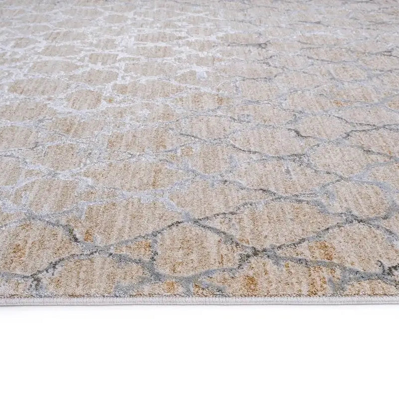 A close-up of a textured area rug with a geometric, cracked stone pattern in beige, cream, and light gray.