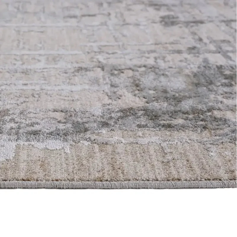 A close-up of a distressed area rug with a textured, vintage pattern in shades of beige, gray, and off-white, showing the pile and fringed edge.