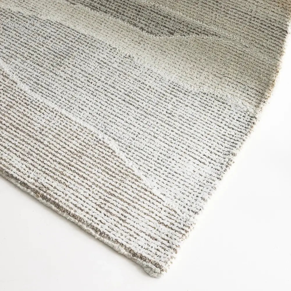 A close-up of a textured area rug with a horizontal striped pattern in shades of gray, beige, and off-white, shown on a clean white background.