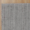 A close-up of a textured woven area rug in a heathered gray and white tone, shown on a light wood floor.