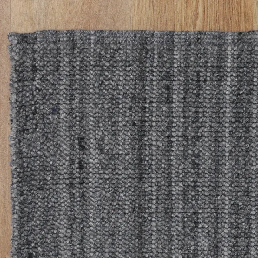 A close-up of a dark gray textured woven rug with a ribbed pattern, shown on a light wood floor.